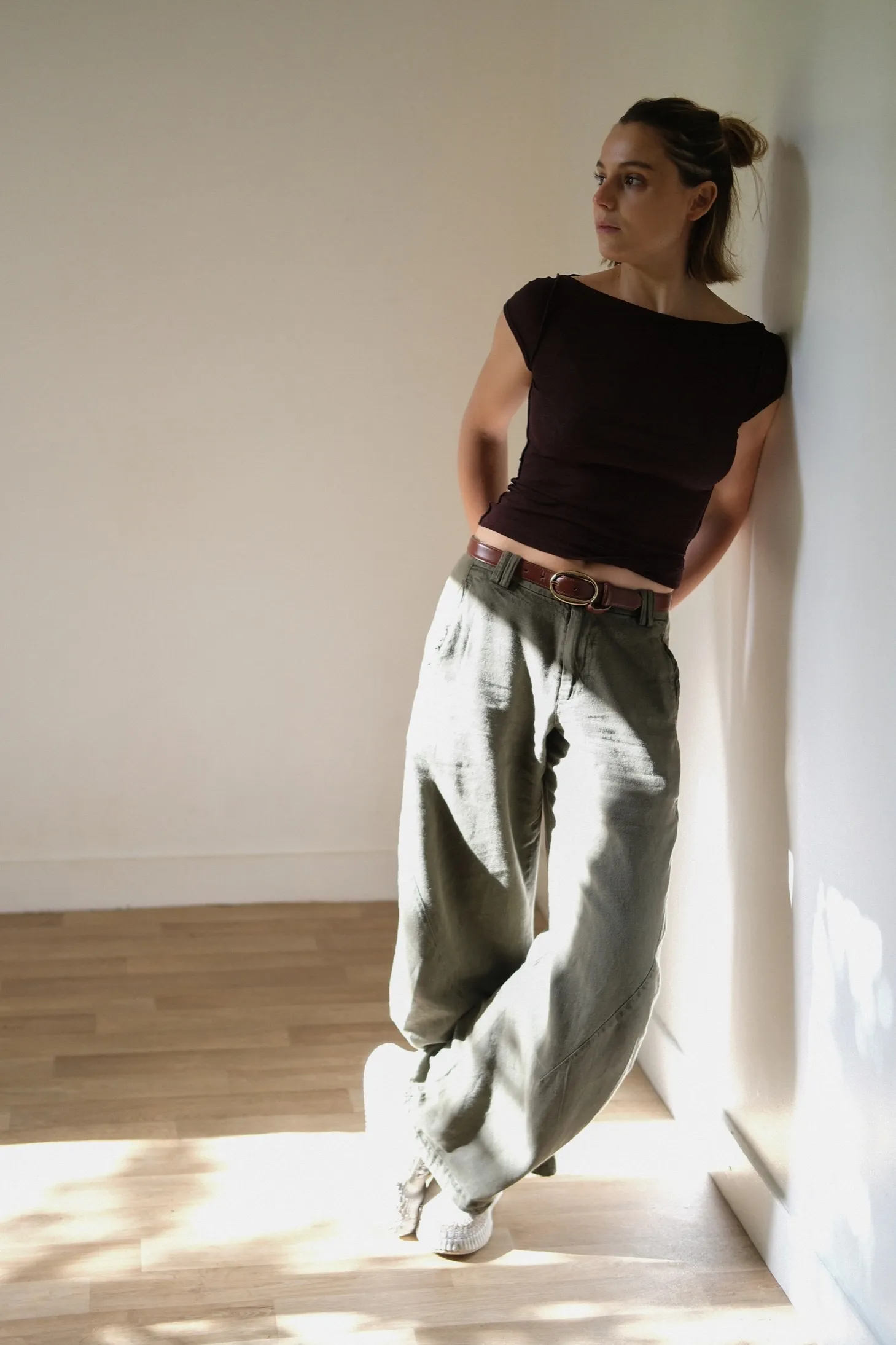 Louise Charnallet en pied, adossée à un mur clair, dans la lumière du jour.